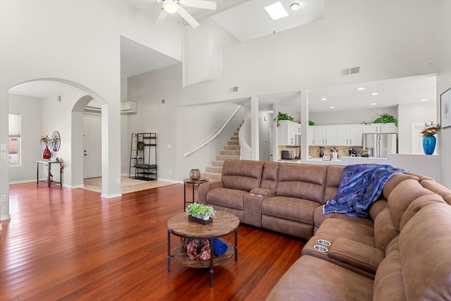 living room featuring ceiling fan, high vaulted ceiling, a skylight, and hardwood / wood-style floors