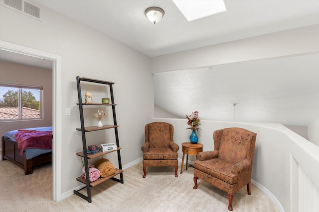 living area featuring a skylight, light carpet, and a textured ceiling