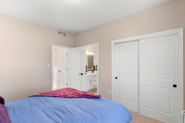 carpeted bedroom with a closet, a textured ceiling, and ensuite bathroom