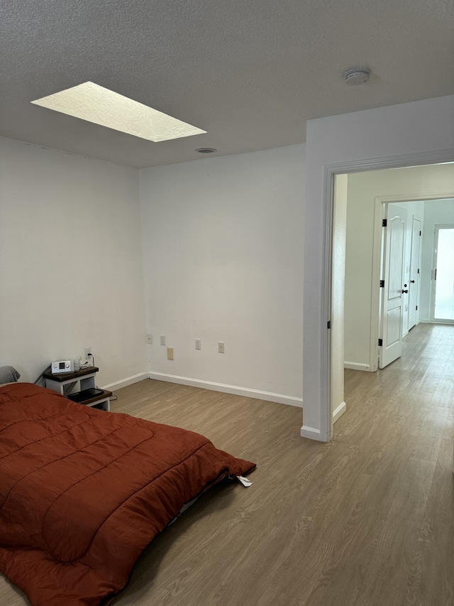 bedroom featuring a textured ceiling, light hardwood / wood-style flooring, and a skylight