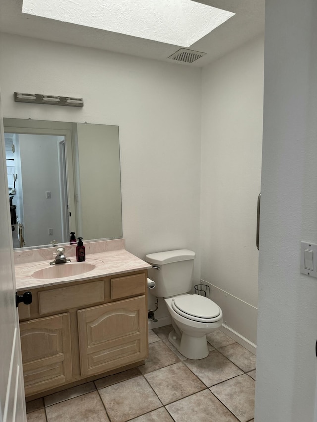 bathroom with toilet, vanity, a skylight, and tile patterned flooring