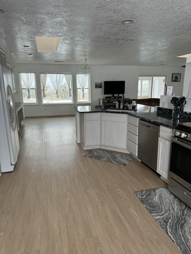 kitchen with kitchen peninsula, light hardwood / wood-style flooring, white cabinetry, a chandelier, and stainless steel appliances