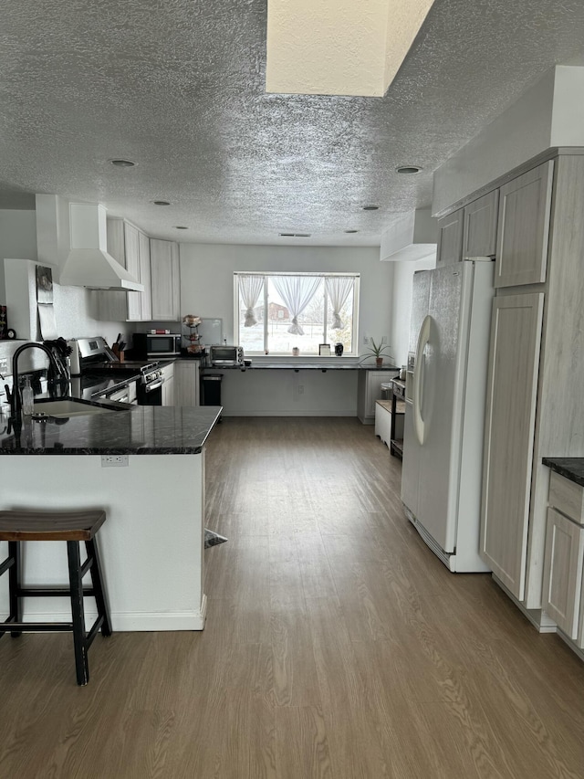 kitchen featuring white refrigerator with ice dispenser, stainless steel range with electric stovetop, sink, kitchen peninsula, and wall chimney exhaust hood