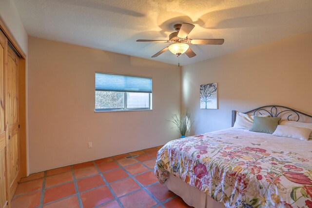 bedroom featuring ceiling fan, a closet, tile patterned floors, and a textured ceiling