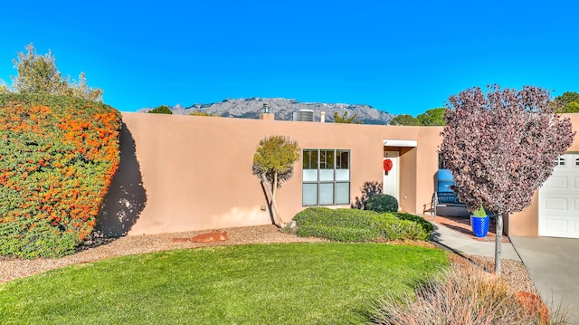 pueblo revival-style home with a mountain view, a front lawn, and a garage