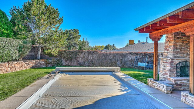 view of swimming pool featuring a yard and an outdoor stone fireplace