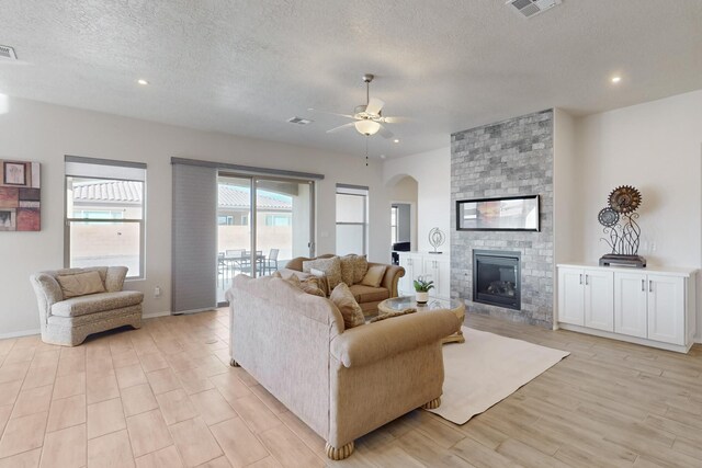 living room with ceiling fan, a textured ceiling, a fireplace, and light hardwood / wood-style floors