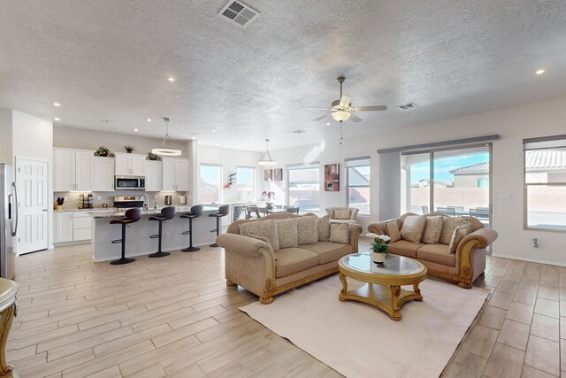 living room with ceiling fan, sink, and a textured ceiling