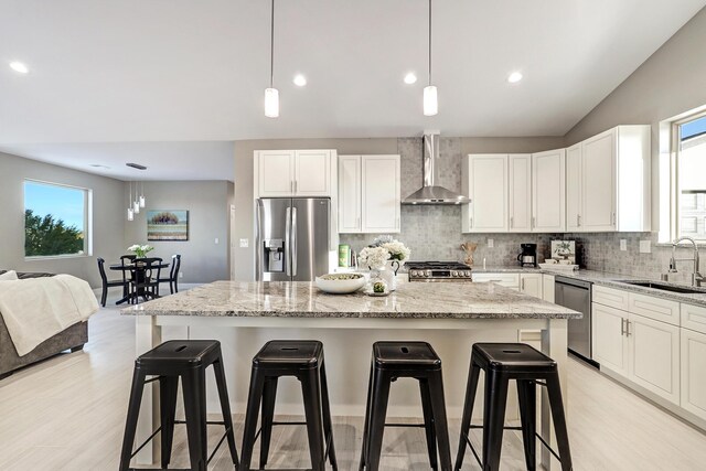 kitchen with a kitchen island, sink, appliances with stainless steel finishes, a kitchen breakfast bar, and wall chimney exhaust hood