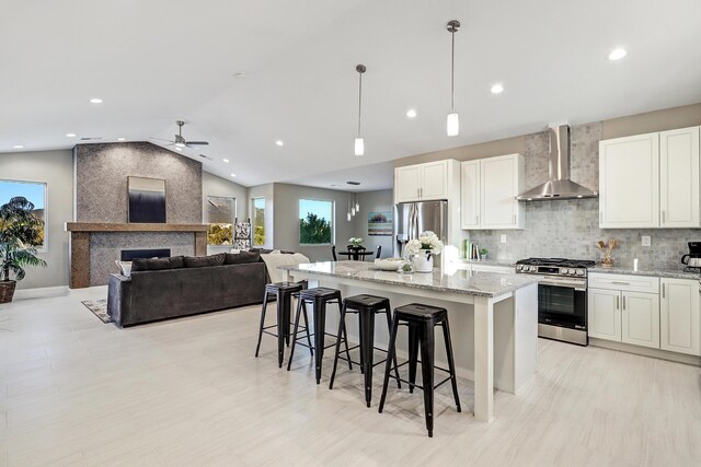 kitchen featuring pendant lighting, lofted ceiling, a kitchen island, wall chimney range hood, and stainless steel appliances