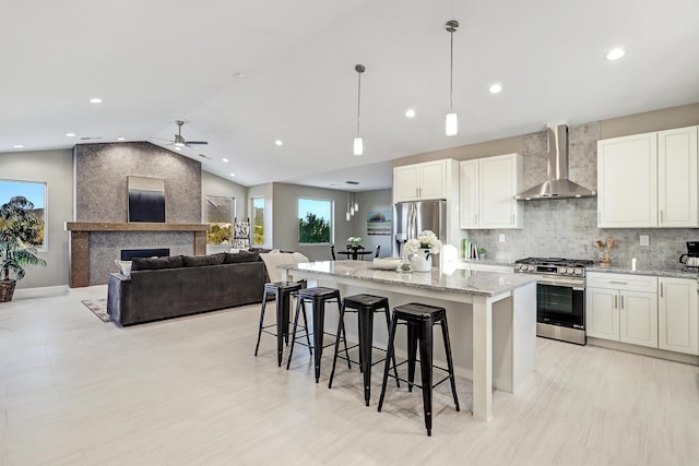 kitchen featuring stainless steel appliances, a kitchen island, white cabinetry, wall chimney range hood, and decorative light fixtures