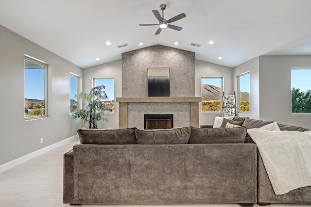 living room with ceiling fan, vaulted ceiling, a fireplace, and light wood-type flooring