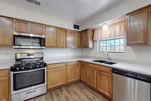 kitchen with appliances with stainless steel finishes, sink, and light hardwood / wood-style floors