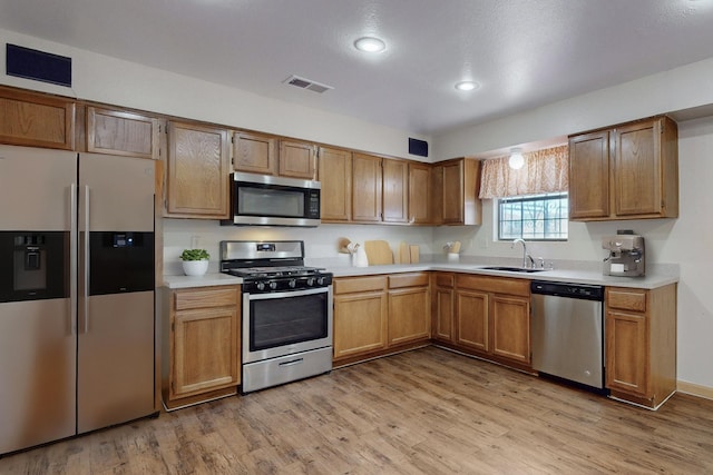 kitchen with appliances with stainless steel finishes, sink, and light hardwood / wood-style flooring