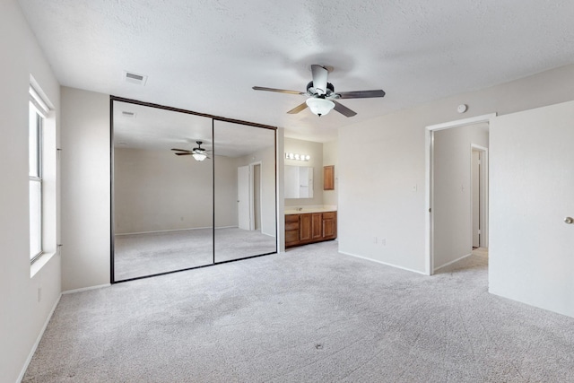 unfurnished bedroom with a textured ceiling, ensuite bath, a closet, ceiling fan, and light colored carpet