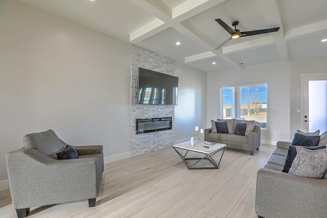 living room with ceiling fan, beam ceiling, a stone fireplace, and coffered ceiling