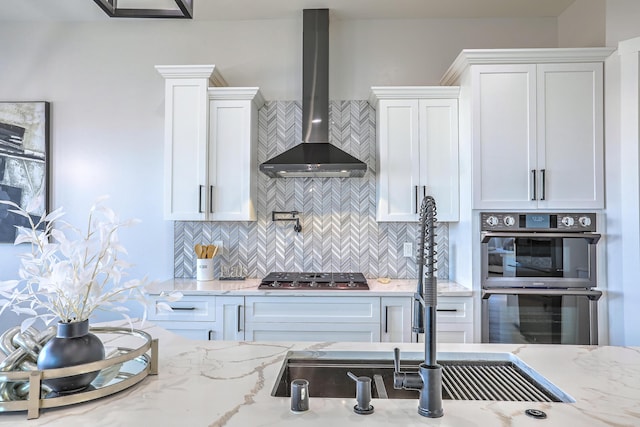 kitchen featuring white cabinetry, stainless steel appliances, tasteful backsplash, light stone countertops, and wall chimney exhaust hood