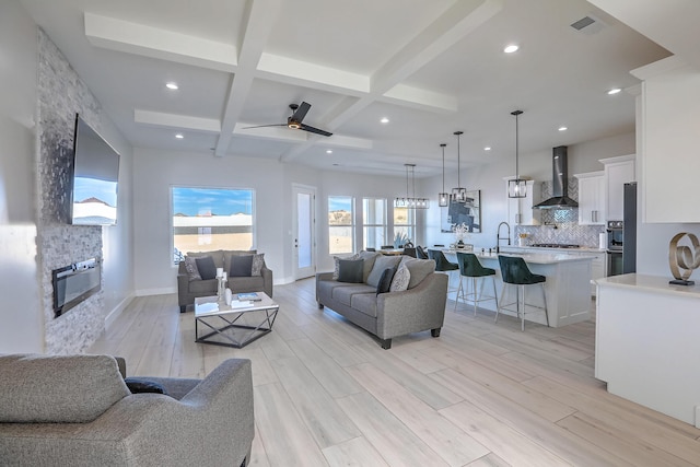 living room with beamed ceiling, a fireplace, sink, light wood-type flooring, and coffered ceiling