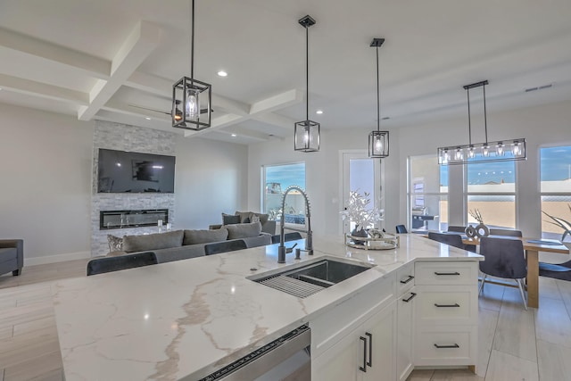 kitchen with coffered ceiling, beamed ceiling, decorative light fixtures, light stone countertops, and sink