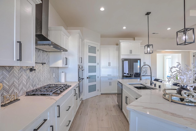 kitchen featuring hanging light fixtures, wall chimney range hood, sink, and white cabinetry