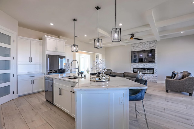 kitchen featuring light stone countertops, decorative light fixtures, white cabinets, and an island with sink