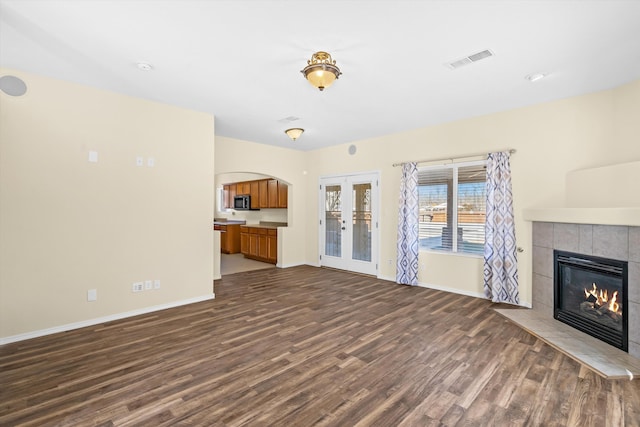 unfurnished living room with french doors, dark wood-type flooring, and a tiled fireplace