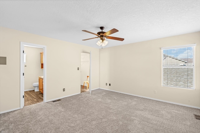 unfurnished bedroom featuring ceiling fan, light colored carpet, connected bathroom, and a textured ceiling