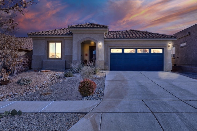 mediterranean / spanish home with a garage, concrete driveway, a tile roof, and stucco siding