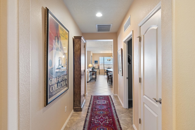 corridor with visible vents, a textured ceiling, baseboards, and light tile patterned floors