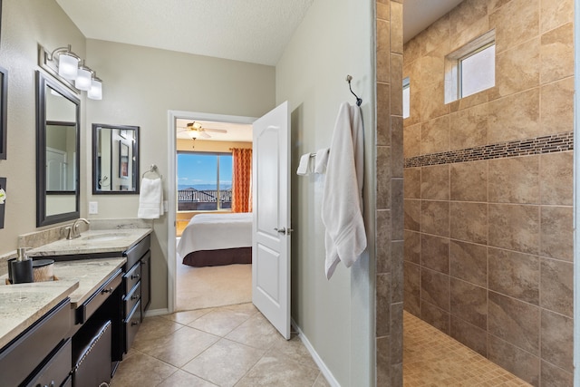 bathroom featuring ceiling fan, vanity, tile patterned floors, tiled shower, and a textured ceiling