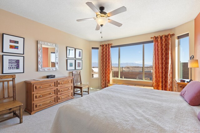 bedroom with ceiling fan, light colored carpet, a mountain view, and a textured ceiling