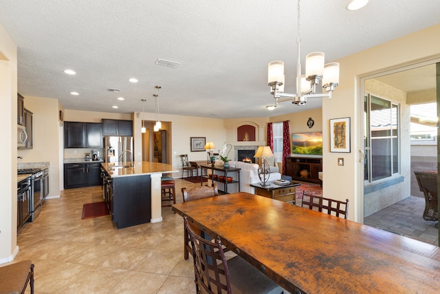 dining space featuring visible vents, an inviting chandelier, a lit fireplace, a textured ceiling, and recessed lighting