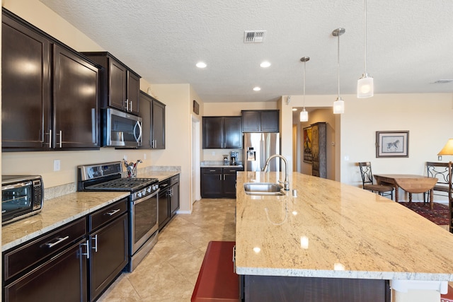 kitchen featuring pendant lighting, stainless steel appliances, an island with sink, sink, and light stone counters