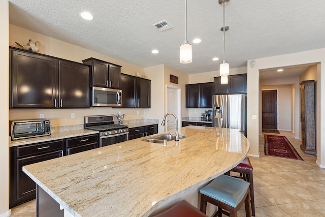 kitchen with appliances with stainless steel finishes, decorative light fixtures, an island with sink, sink, and a breakfast bar area