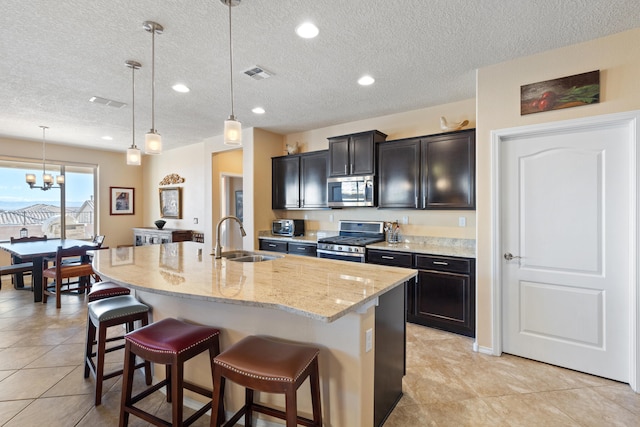 kitchen featuring a center island with sink, stainless steel appliances, decorative light fixtures, a kitchen breakfast bar, and sink