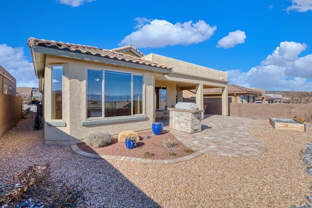 exterior space featuring a patio, an outdoor kitchen, a fenced backyard, a tiled roof, and stucco siding