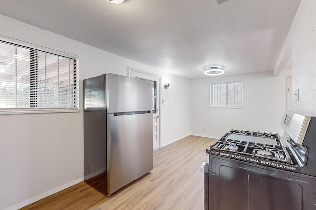 kitchen featuring a textured ceiling, range with gas cooktop, light hardwood / wood-style flooring, and stainless steel refrigerator