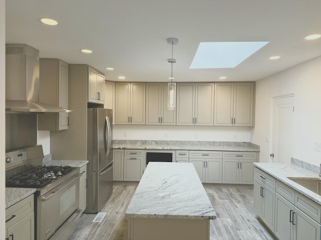 kitchen with light hardwood / wood-style flooring, gray cabinets, appliances with stainless steel finishes, a kitchen island, and wall chimney exhaust hood