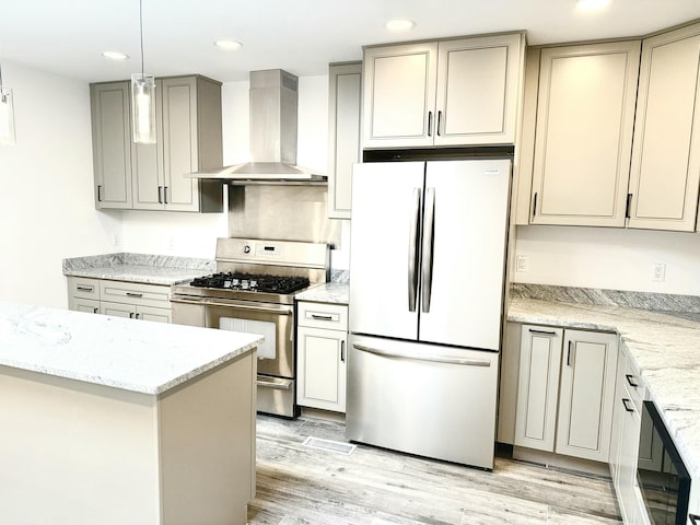 kitchen with appliances with stainless steel finishes, decorative light fixtures, wall chimney exhaust hood, light stone counters, and light hardwood / wood-style flooring