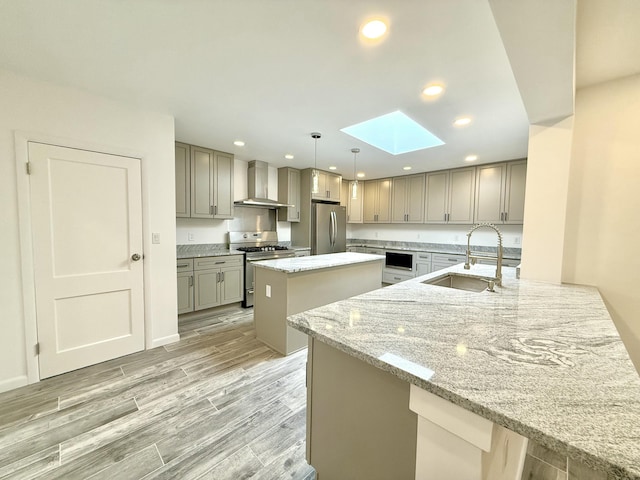 kitchen featuring appliances with stainless steel finishes, pendant lighting, sink, light stone counters, and wall chimney range hood