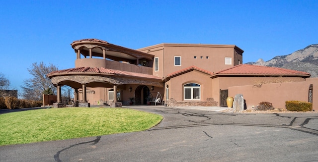 rear view of property with a lawn, aphalt driveway, a tiled roof, a mountain view, and stucco siding