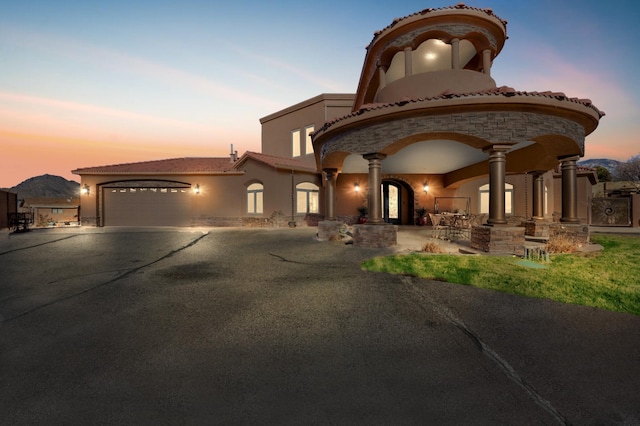 exterior space with aphalt driveway, stone siding, an attached garage, and stucco siding