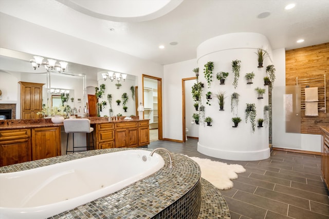 full bathroom featuring a notable chandelier, a fireplace, vanity, and a bath