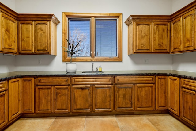 kitchen featuring dark stone countertops, a sink, light tile patterned flooring, and brown cabinets