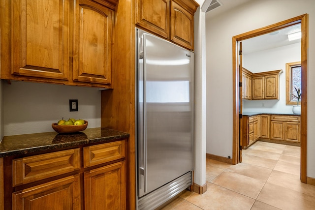 kitchen featuring built in fridge, visible vents, brown cabinets, dark stone countertops, and light tile patterned flooring