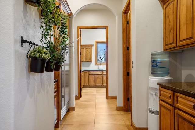 hall featuring arched walkways, baseboards, and light tile patterned floors