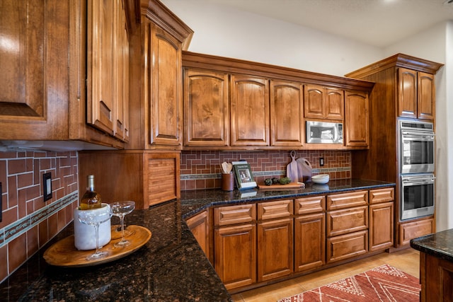 kitchen with light tile patterned flooring, stainless steel appliances, decorative backsplash, dark stone counters, and brown cabinetry