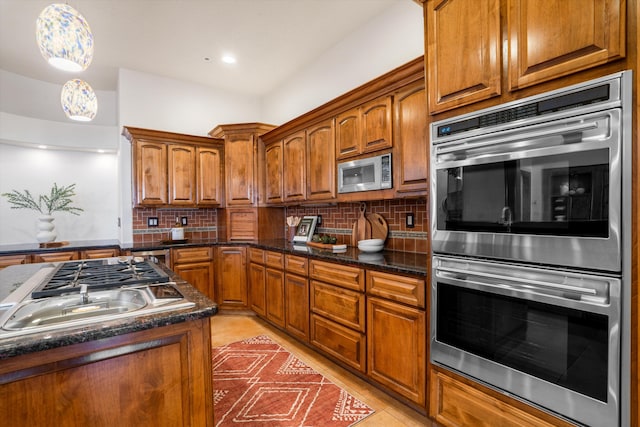 kitchen with appliances with stainless steel finishes, tasteful backsplash, brown cabinets, and light tile patterned floors