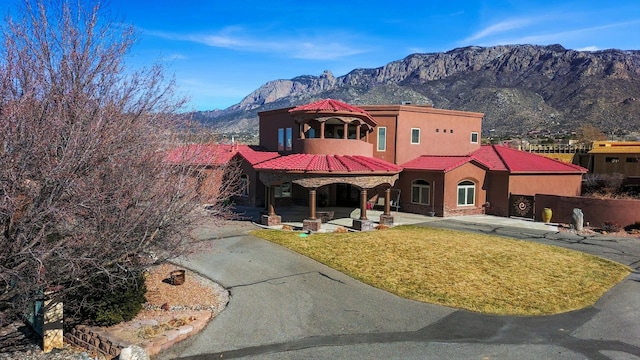 mediterranean / spanish home with a tiled roof, a front yard, a mountain view, and stucco siding