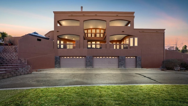 view of front of house featuring a garage, stone siding, driveway, and stucco siding